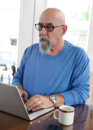 Man working on laptop at kitchen table.